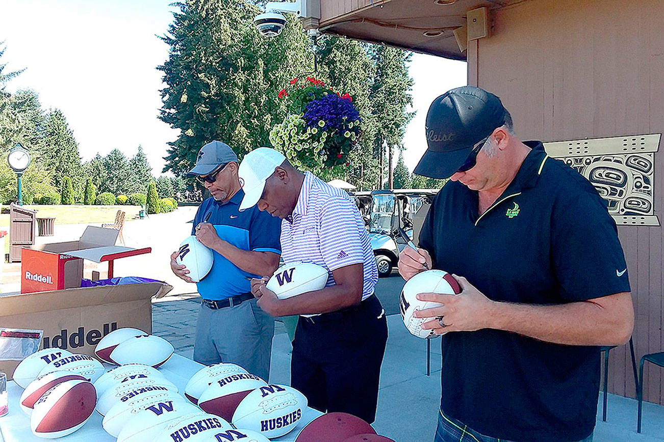 Pierre LaBossiere/Peninsula Daily News
From left, former UW Huskies Mark Lee, Ronnie Rowland and Jason Chorak sign footballs for an auction at Cedars at Dungeness in Sequim on Thursday as part of the Sonny Sixkiller Celebrity Golf Classic.
