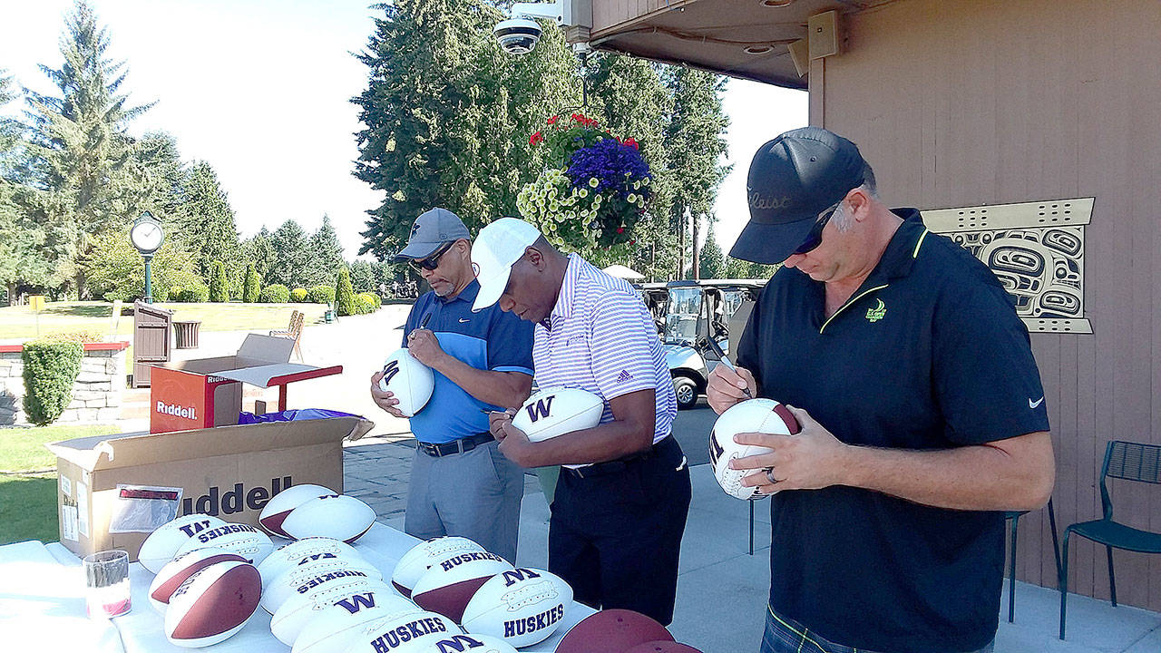 Pierre LaBossiere/Peninsula Daily News From left, former UW Huskies Mark Lee, Ronnie Rowland and Jason Chorak sign footballs for an auction at Cedars at Dungeness in Sequim on Thursday as part of the Sonny Sixkiller Celebrity Golf Classic.