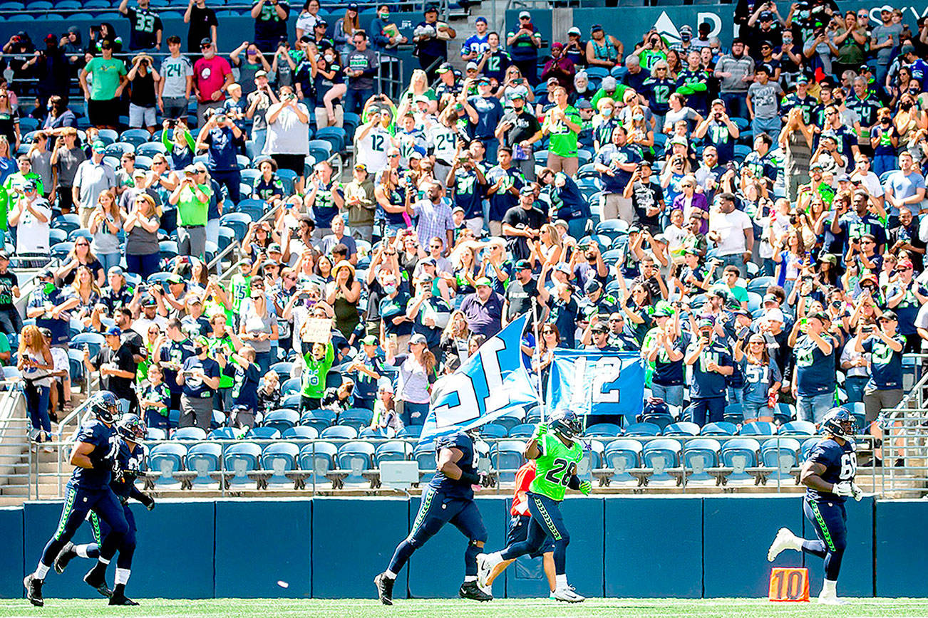 Seattle Seahawks cornerback Ugo Amadi carries the 12 flag out to cheering fans before playing a mock game as part of an NFL football training camp at Lumen Field in Seattle, Sunday, Aug. 8, 2021. (Bettina Hansen/The Seattle Times via AP)