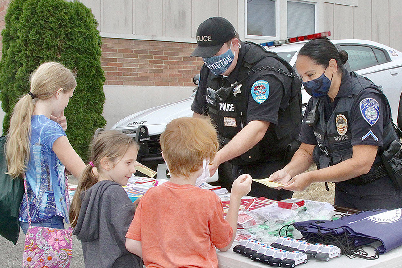 Police officers Adam Lovik and Swift Sanchez help a bunch of school children with information and freebie from the police department. The Back to school fair, the 13th annual,  was held in the parking lot of the PA school district buildings at 9th and “B” Streets. Over 50 volunteers from many community organizations helped droves of young kids getting ready for school in a few weeks with supplies and information about the upcoming school year which in Port Angeles begins on Sept 2nd this year.