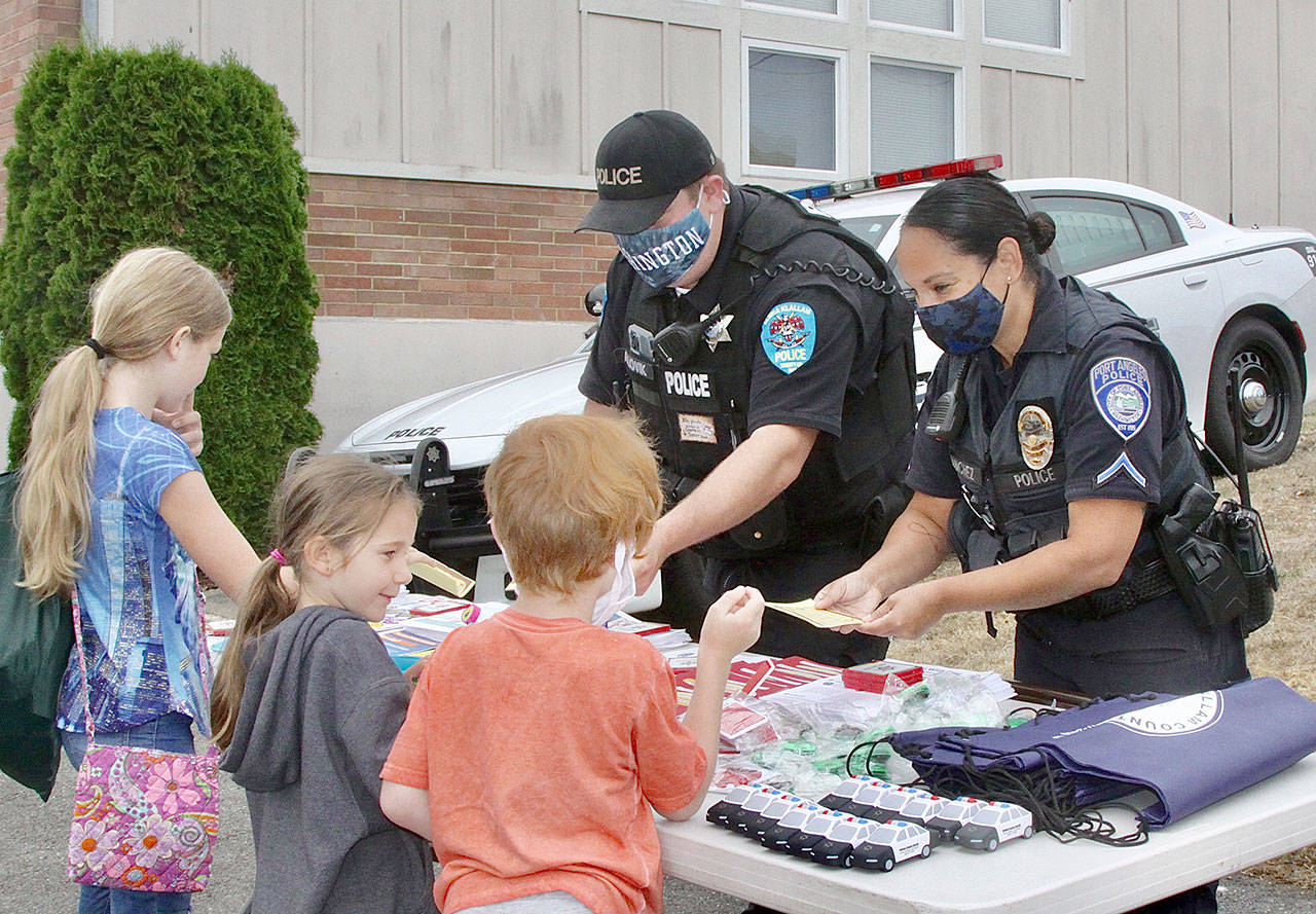 Police officers Adam Lovik and Swift Sanchez help children with information and freebies from the police department at the 13th annual Back to School Fair, held in the parking lot of the Port Angeles School District buildings at Ninth and B Streets. Over 50 volunteers from community organizations helped droves of kids get ready for school with supplies and information about the upcoming school year, which begins Sept. 2 in Port Angeles. (Dave Logan/For Peninsula Daily News)