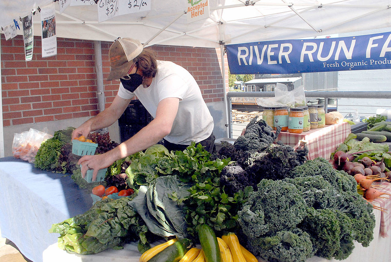 Ben Rutherford, an employee of River Run Farm near Sequim, arranges locally grown produce at the Port Angeles Farmers Market. Such markets are among the destinations in this month’s “Eat Local First” campaign. (Keith Thorpe/Peninsula Daily News)