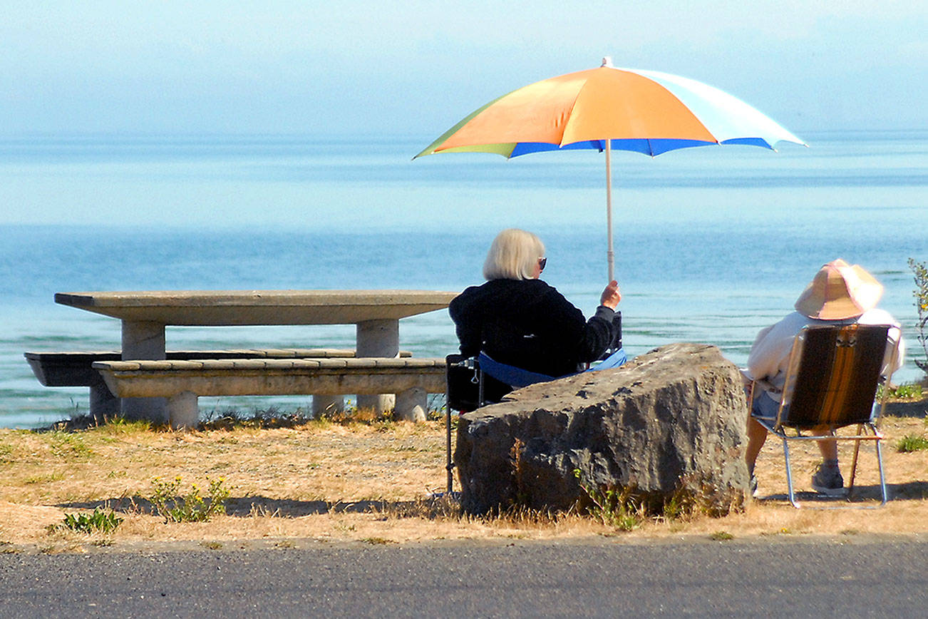 Kathleen Krecklow sits under an umbrella as she converses with Jo Ehly on the shore of Dungeness Bay at Dungeness Landing County Park on Wednesday. The women, both of Sequim, were sharing the morning with other friends in a weekly gathering. (Keith Thorpe/Peninsula Daily News)