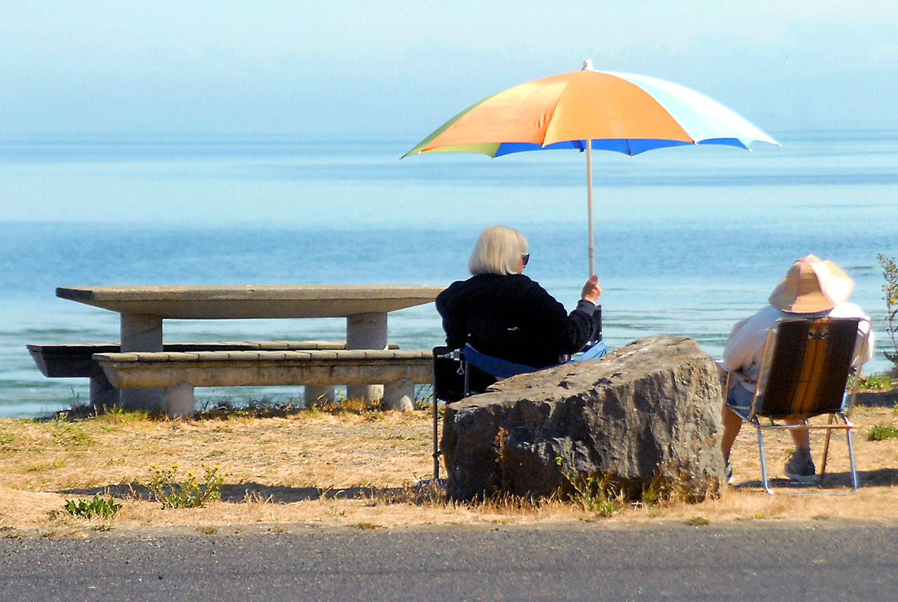 Kathleen Krecklow sits under an umbrella as she converses with Jo Ehly on the shore of Dungeness Bay at Dungeness Landing County Park on Wednesday. The women, both of Sequim, were sharing the morning with other friends in a weekly gathering. (Keith Thorpe/Peninsula Daily News)