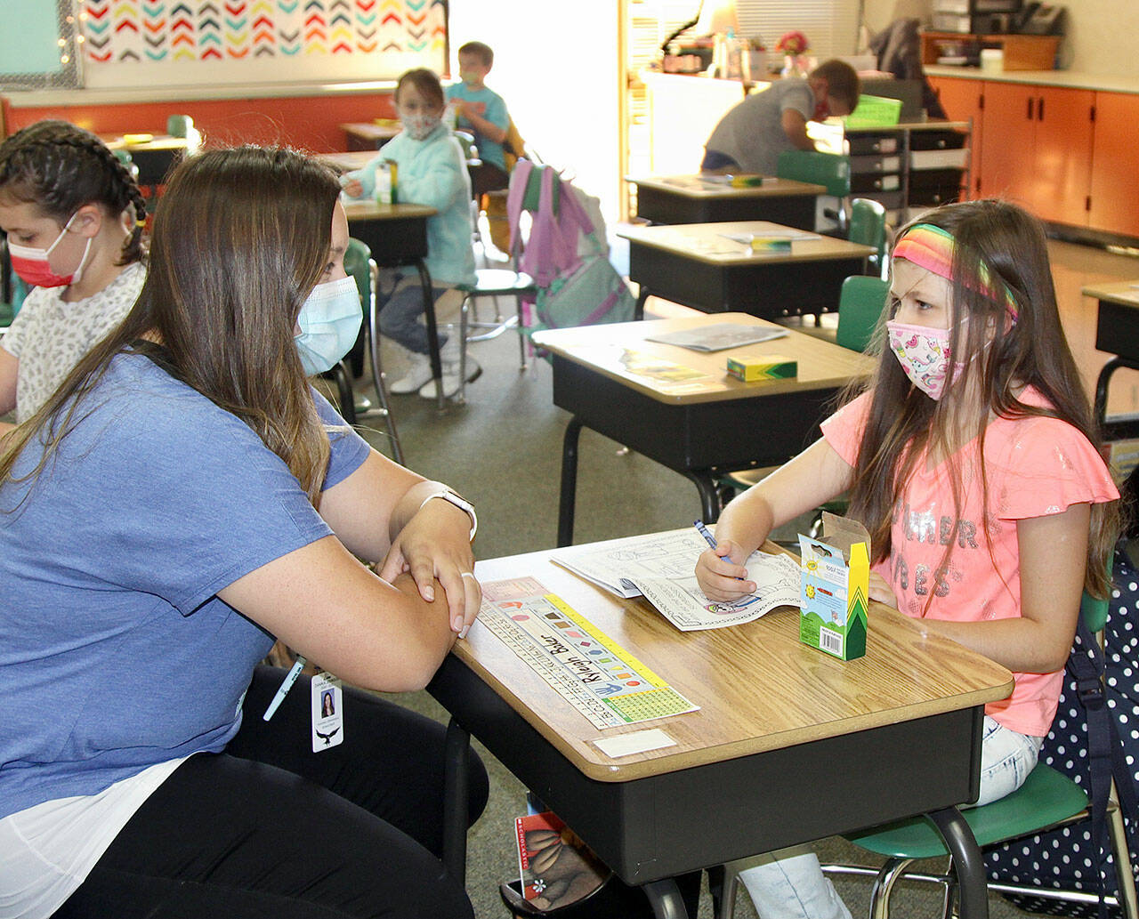 Ryleigh Baker talks with her new teacher, Mrs. Johnson, in the beginning moments of the school day. Each student was given crayons and a coloring book to engage them until everyone arrived. (Dave Logan/For Peninsula Daily News)