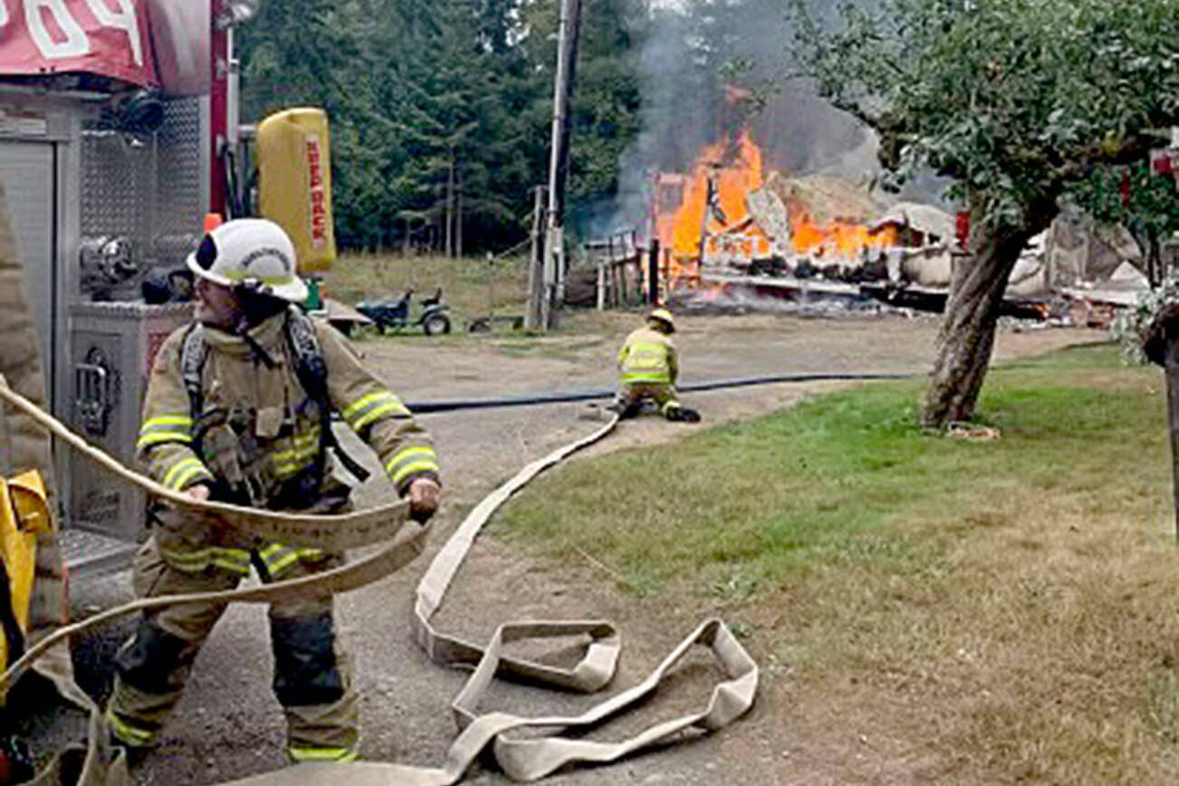 Clallam County Fire District 4 Assistant Fire Chief Alex Baker rolls out a hose Sunday to fight a fire west of Joyce while firefighter Brett Frantz sets up and gets ready for water. (Clallam County Fire District 4)