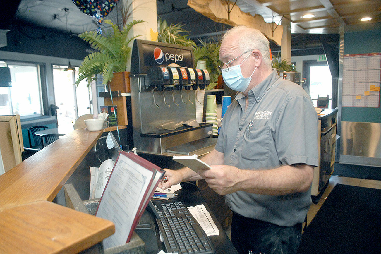 Rick Mathis, owner of Smuggler’s Landing Restaurant & Lounge in Port Angeles, tallies a customer’s bill on Tuesday. (Keith Thorpe/Peninsula Daily News)