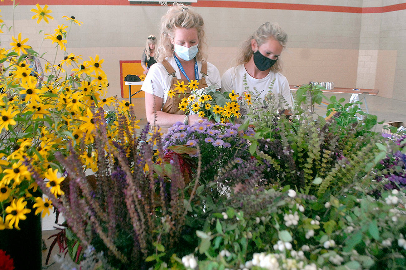Sisters Jenny Edwards, left, and Julia Ahrndt, both of Port Angeles, assemble flower bouquets that will be distributed to teachers and staff members of the Port Angeles School District at an assembly session with volunteers on Thursday at Hamilton School. The pair collected more than 4,000 flowers from their own flower farms, along with donations from other farms and area gardeners, that will be arranged in tin can vases and given out in the days to come to about 450 school district employees as a token of thanks for their hard work in tending to the needs of children. (Keith Thorpe/Peninsula Daily News)