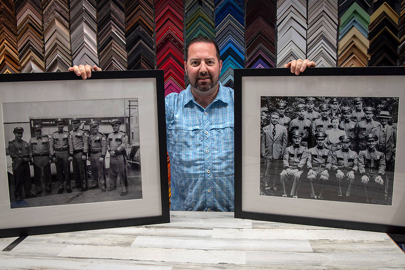 Damon Stamoolis of Sequim’s Clear Image Custom Framing and Photo holds up two of the historic images he digitally cleaned, printed, and framed for the Port Angeles Police Department. Emily Matthiessen/Olympic Peninsula News Group