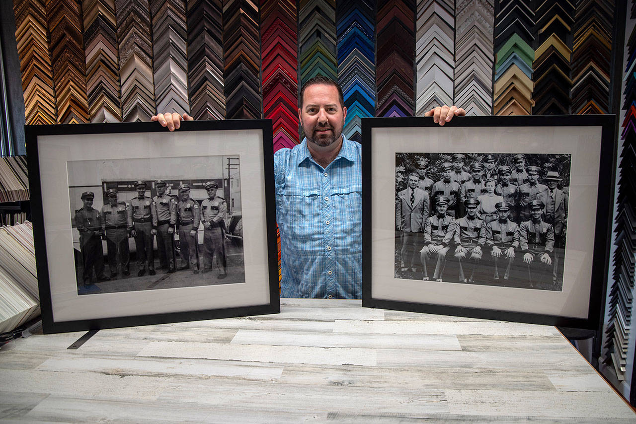 Damon Stamoolis of Sequim’s Clear Image Custom Framing and Photo holds up two of the historic images he digitally cleaned, printed, and framed for the Port Angeles Police Department. (Emily Matthiessen/Olympic Peninsula News Group)