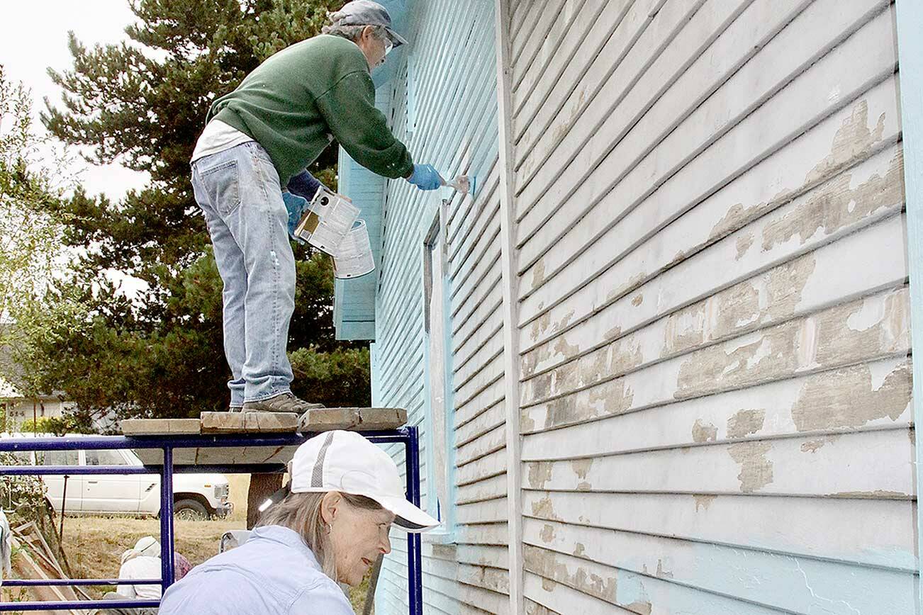 Paul Stutseman, on scaffolding, and Ardith Hansel, foreground, paint a house as part of a church project. (Dave Logan/For Peninsula Daily News)