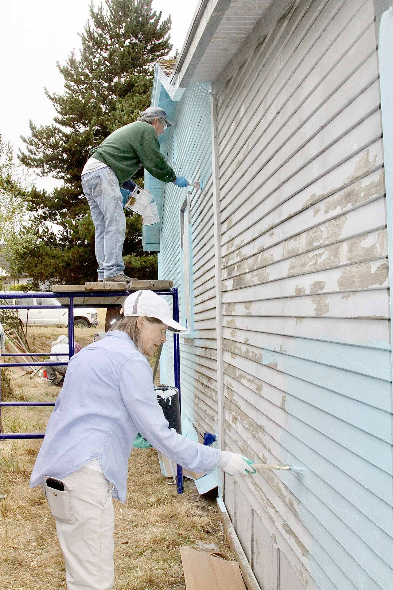 Paul Stutseman, on scaffolding, and Ardith Hansel, foreground, paint a house as part of a church project. (Dave Logan/For Peninsula Daily News)