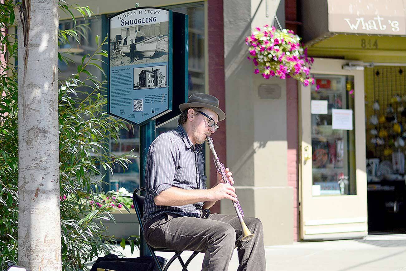 Busker Jonathan Doyle plays on Water Street in Port Townsend beside the Hidden History sign about smuggling during the 19th and 20th centuries. The series of Hidden History panels inspire twice-monthly walking tours around downtown. (Diane Urbani de la Paz/Peninsula Daily News)