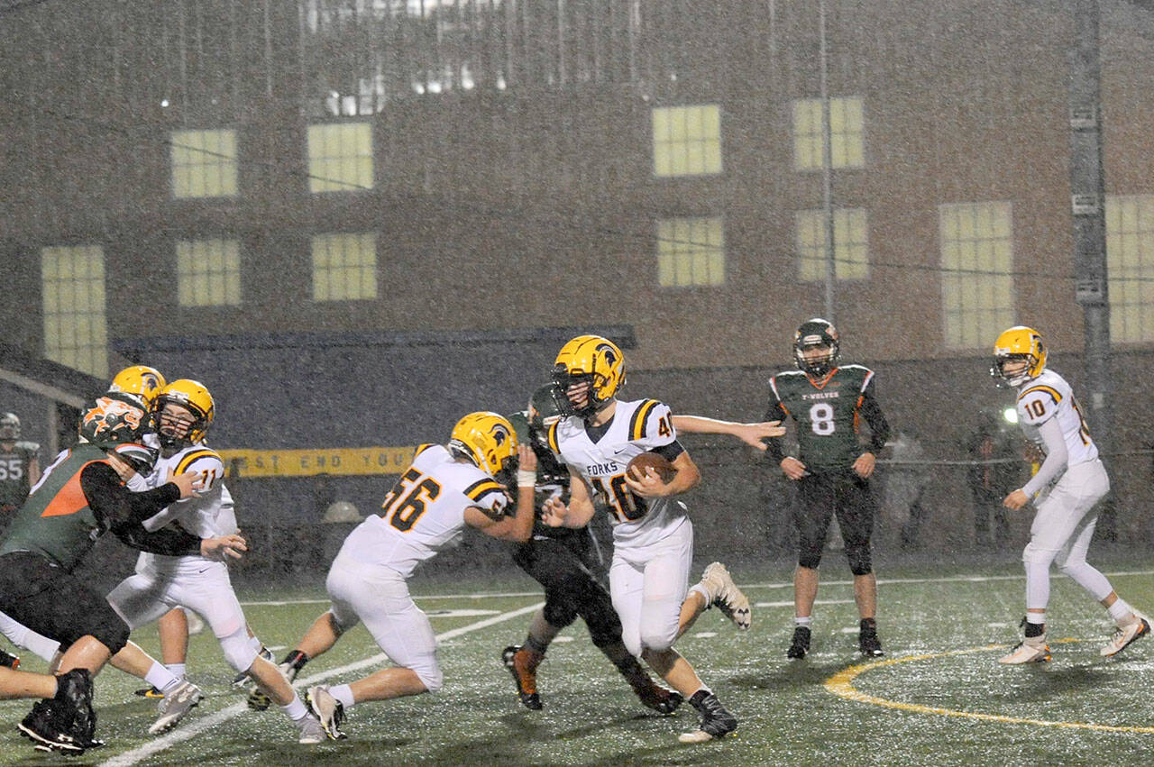 Forks running back Nate Dahlgren (40) picks up yardage during a deluge behind the blocking of Conner Earls (56) and Kalab Blanton (11). (Lonnie Archibald /for Peninsula Daily News)