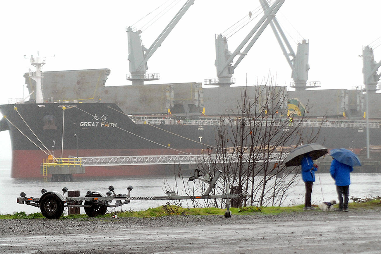 Debbi and Richard Szabo of Port Angeles, along with their dog, Tipsy, walk along the Port Angeles Waterfront as the bulk carrier Great Faith takes on cargo in the rain at the Port of Port Angeles Terminal 3 on Thursday. Unsettled weather is expected across the region through the weekend. (Keith Thorpe/Peninsula Daily News)