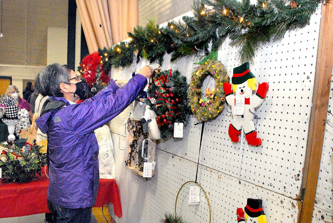 Marla Tolliver of Neah Bay examines wreaths and hanging holiday decorations on Saturday at the annual Christmas Cottage craft fair at Vern Burton Community Center in Port Angeles. The free event, which continues Sunday from 10 a.m. to 4 p.m., features a wide variety of holiday crafts created by a collection of local artists and artisans. (Keith Thorpe/Peninsula Daily News)