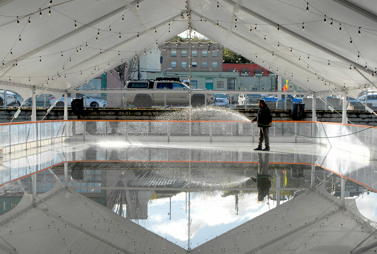 Shawn Kidwell, an employee of Ice-America, a California-based company that rents portable ice rinks, applies water on Tuesday to the refrigerated surface of a temporary rink that will be the highlight of the Port Angeles Winter Ice Village. (Keith Thorpe/Peninsula Daily News)