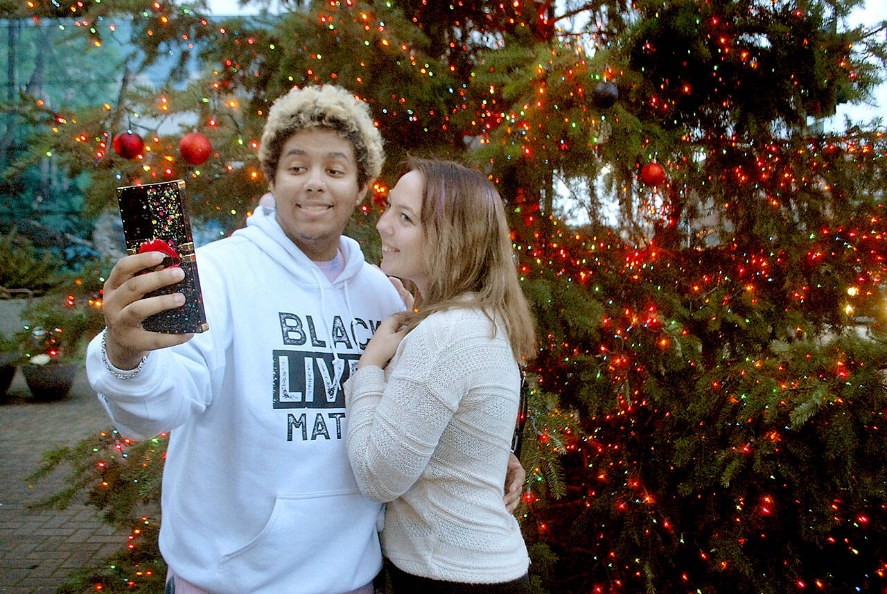 Julyan Hardeman and Sebrena Merly, both of Longview, take a selfie in front of the Christmas tree at the Conrad Dyar Memorial Fountain in downtown Port Angeles on Wednesday. The tree, adorned with about 10,000 miniature lights and several dozen ornaments added later, will oversee the downtown area through the holidays. (Keith Thorpe/Peninsula Daily News)