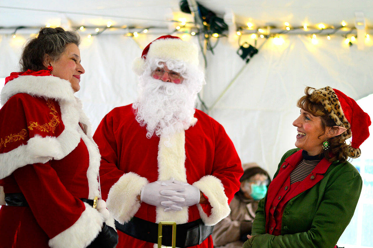Santa Claus, surrounded by Mrs. Claus, left, and Kimberly the Elf, greeted community members of all ages on Saturday under the Tyler Street Plaza tent in downtown Port Townsend. Santa, known at other times of year as Nathan Barnett; Mrs. Claus, aka Cindy Madsen and Kimberly Snow — “that’s my real name” — were part of the Main Street Program’s seasonal activities. “With the holidays, the diet is not going well,” Barnett admitted, “but Mrs. Claus is getting me an exercise program for Christmas.” (Diane Urbani de la Paz/Peninsula Daily News)