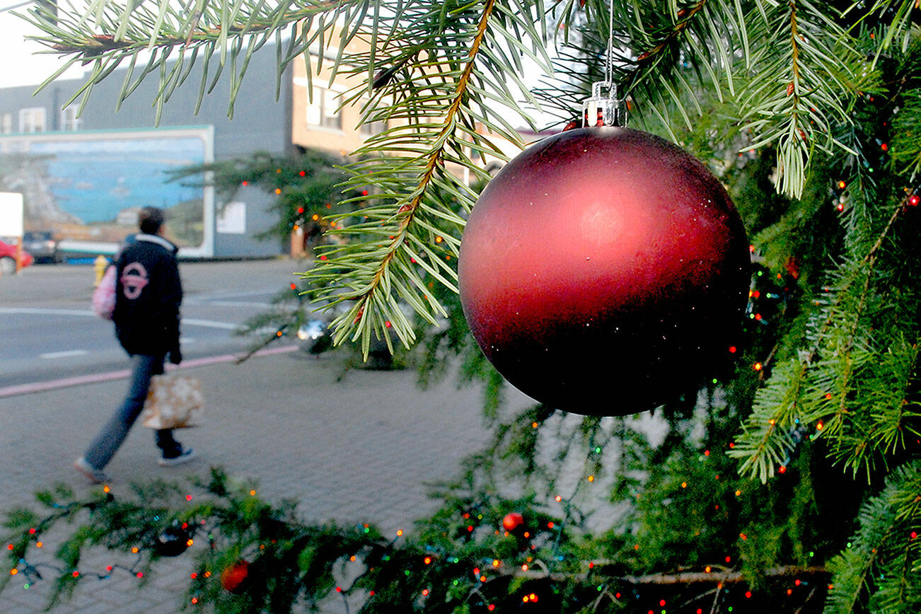 An ornament hangs from the Christmas tree in downtown Port Angeles on Tuesday as a pedestrian walks past the Conrad Dyar Memorial Fountain plaza. The tree, adorned with about 10,000 miniature lights, will remain at the plaza into early January. (Keith Thorpe/Peninsula Daily News)