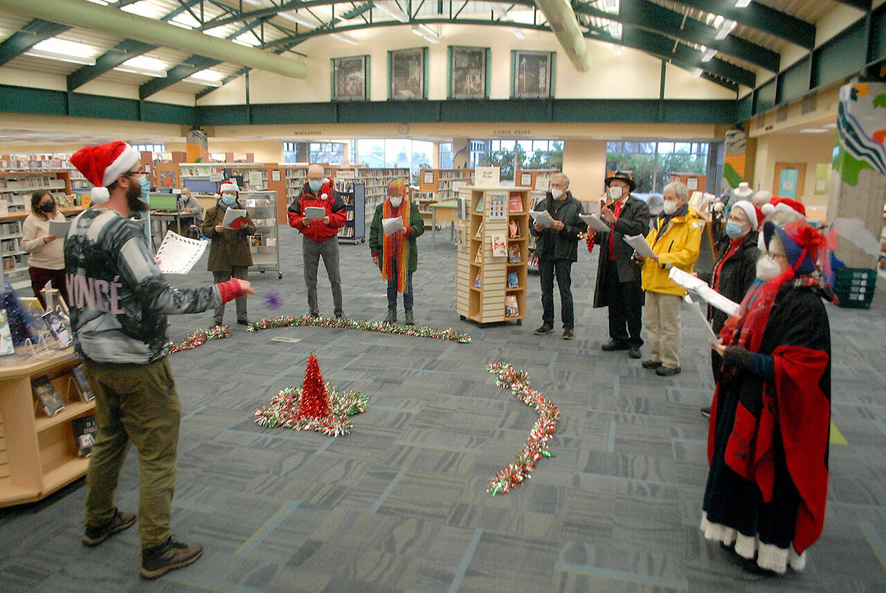 Noah Smith, director of music ministry at Holy Trinity Lutheran Church, with hat at left, directs a collection of carolers from the church during a performance of holiday songs at the Port Angeles Public Library on Saturday. The church plans to hold virtual and in-person candlelight services on Christmas Eve. For more information, visit www.go2trinity.org. (Keith Thorpe/Peninsula Daily News)