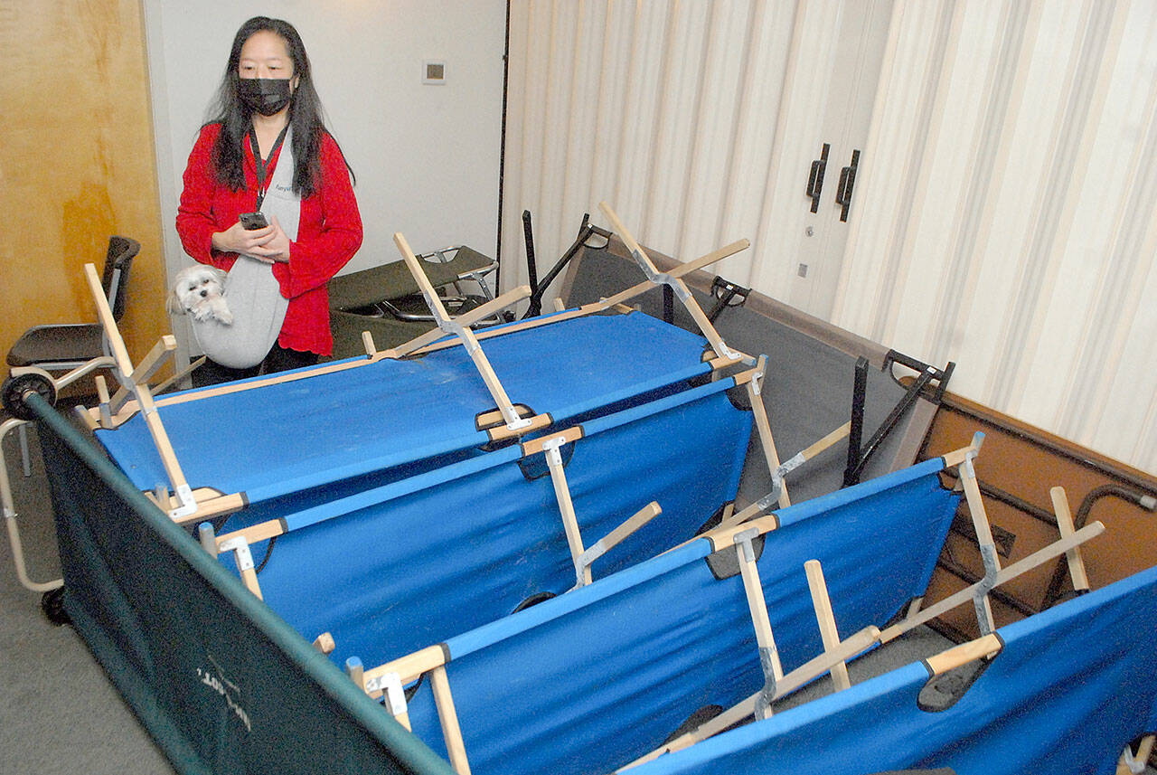 Serenity House shelter director Michele Lefebvre, along with her dog, Lei, looks over a few of the cots that can be deployed to accommodate people seeking relief from cold weather. (Keith Thorpe/Peninsula Daily News)