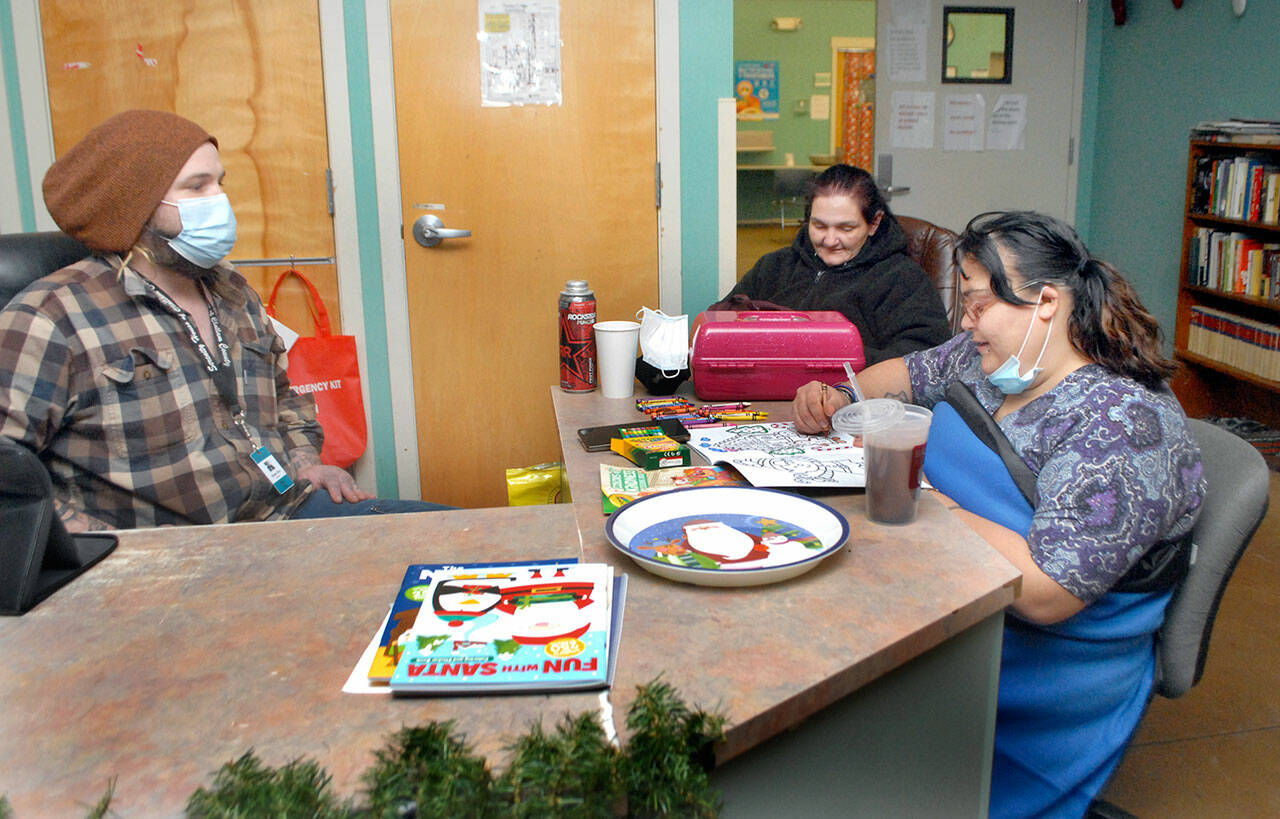 Serenity House shelter Mike Wiley (left) sits at the front desk with clients Debra Roberts and Renee Mata (right) preparing for a week of cold weather at the Port Angeles homeless shelter on Saturday.  (Keith Thorpe / Peninsula Daily News)