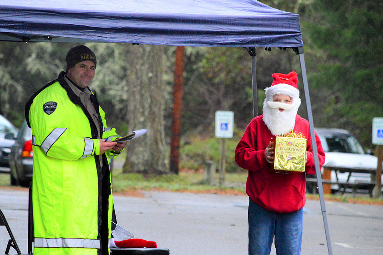 Jefferson County Sheriff's Department Sgt. Andy Pernsteiner, left, and Daltry Lammers, 12, of Chimacum greeted droves of people outside the Tri-Area Community Center in Chimacum on Saturday afternoon, where volunteers dished up 498 Christmas meals to go. Many people made reservations, organizer Rita Hubbard said, but quite a few called on Christmas Day asking if they could have a takeout dinner. "Come right now and we'll get you fed," Hubbard told the last-minute callers.  Diane Urbani de la Paz/Peninsula Daily News