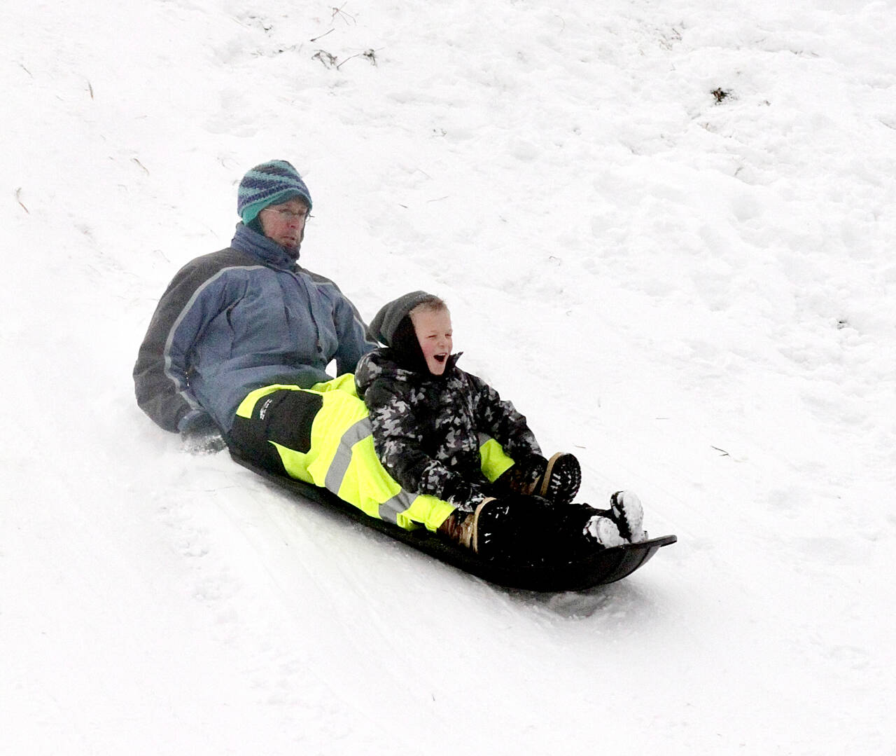Ned Hammer and his son, Sam Lubinski-Hammer, 7, slide down a popular hill at Stevens Middle School in Port Angeles on Monday morning when the temperature was 19 degrees. (Dave Logan/for Peninsula Daily News)