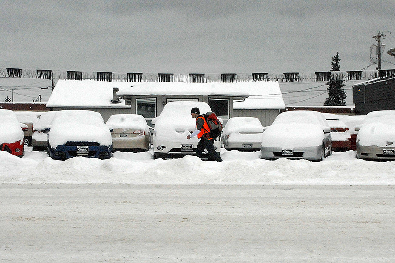 A pedestrian walks past a line of snow-covered vehicles on the lot of Randy’s Auto Sales in the 800 block of East First Street in Port Angeles on Tuesday. A small amount of overnight snow added to previous snowfalls that began on Christmas Day along most of the North Olympic Peninsula. (Keith Thorpe/Peninsula Daily News)