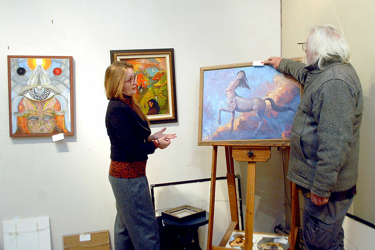 Keith Thorpe/Peninsula Daily News
Bob Stokes, owner of Studio Bob in Port Angeles, right, affixes a sold tag to the oil painting "Sagittarius" by Daniel Miller as Port Angeles artist Sarah Tucker helps on Thursday to prepare for this weekend's "Bring Your Own Art" exhibition.