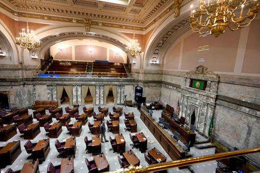 A lone worker walks on the floor of the state Senate last Thursday at the Capitol in Olympia as the room was being prepared for the start of the 2022 legislative session, which opened Monday. The new session will look much like the one a year ago: a limited number of lawmakers on site at the Capitol, and committee hearings being fully remote due to the ongoing COVID-19 pandemic. (Ted S. Warren/The Associated Press)