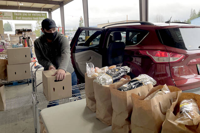 Scott Gardinier/Peninsula Daily News 
Port Angeles Food Bank workers hand out bags of food supplies and sanitization products to a long line of cars Wednesday afternoon. More than 90 people came to the drive-thru by 2 p.m. The food bank is currently preparing an indoor shopping area that is expected to be open early this year.