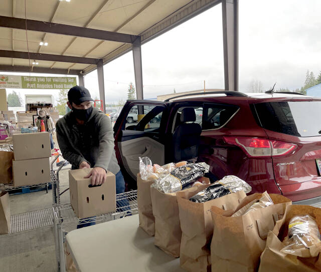 Port Angeles Food Bank workers hand out bags of food supplies and sanitization products to a long line of cars Wednesday afternoon. More than 90 people came to the drive-thru by 2 p.m. The food bank is currently preparing an indoor shopping area that is expected to be open early this year. (Scott Gardinier/Peninsula Daily News)