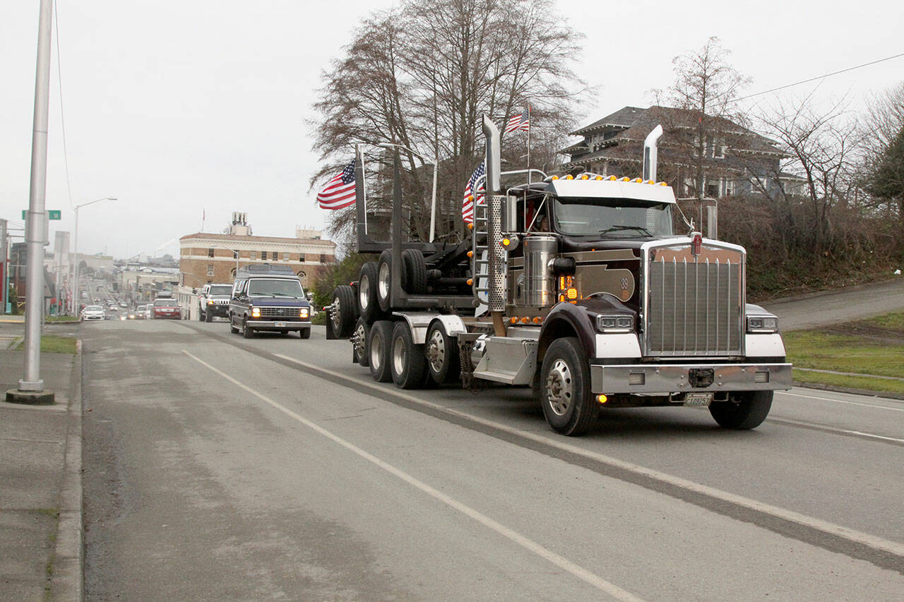 Dan Conner of Port Angeles leads a convoy of more than 20 cars and trucks up First Street as they begin a drive — displaying signs, honking horns and flashing lights — from “Port to Port” from Port Angeles to Port Townsend and back on Saturday morning. (Dave Logan/for Peninsula Daily News)
