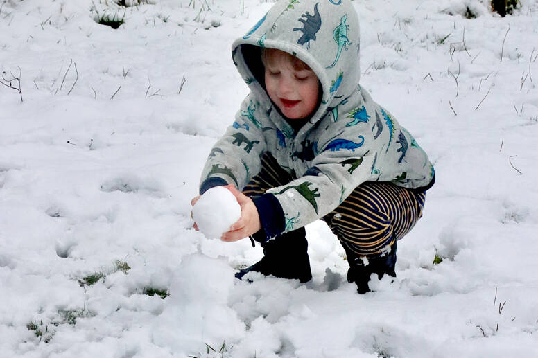 Grayson Haag, 3, helps make a small snowman Thursday morning from his home on Peabody Street. His mom, Amber Garbrick, helped with the fun in the snow. (Dave Logan/for Peninsula Daily News)