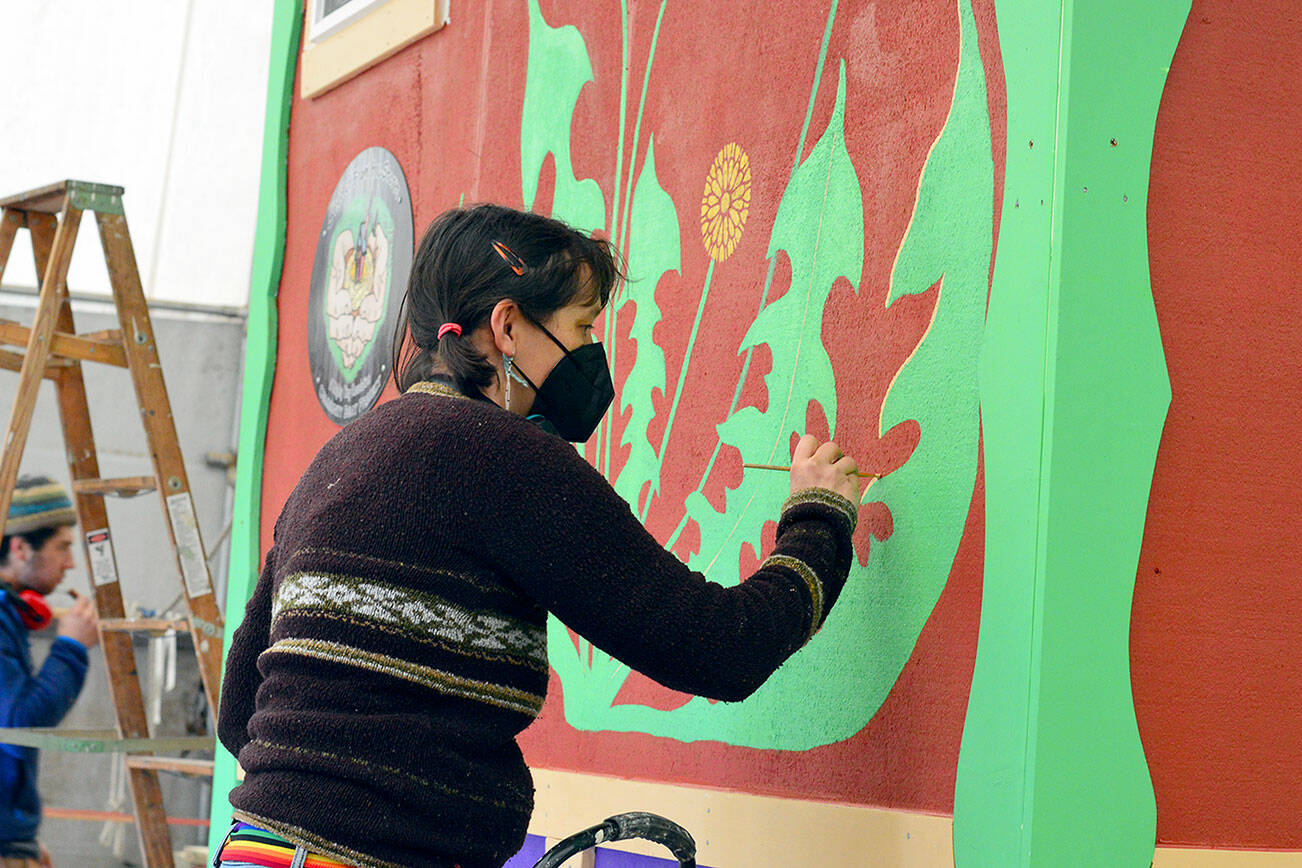Muralist Danielle Fodor paints the newest tiny home, named Meadow Manor, at the Community Boat Project shop in Port Hadlock on Tuesday. The 160-square-foot home is an example of the housing to be built for farmworkers in Chimacum. (Diane Urbani de la Paz/Peninsula Daily News)