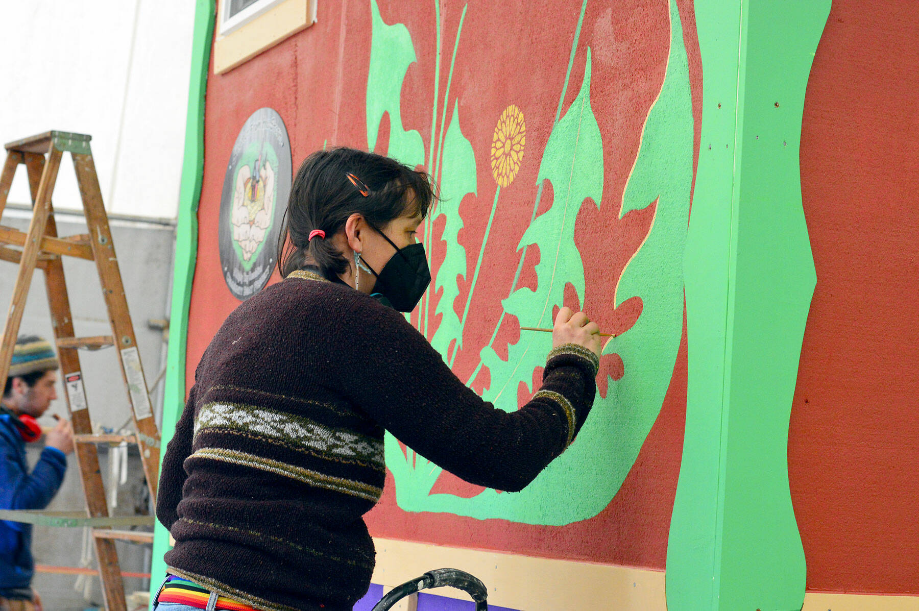 Muralist Danielle Fodor paints the brand new tiny house, named Meadow Manor, at the Community Boat Project store in Port Hadlock on Tuesday.  The 160 square foot house is an example of the housing to be built for the Chimacum farm workers.  (Diane Urbani de la Paz/Peninsula Daily News)