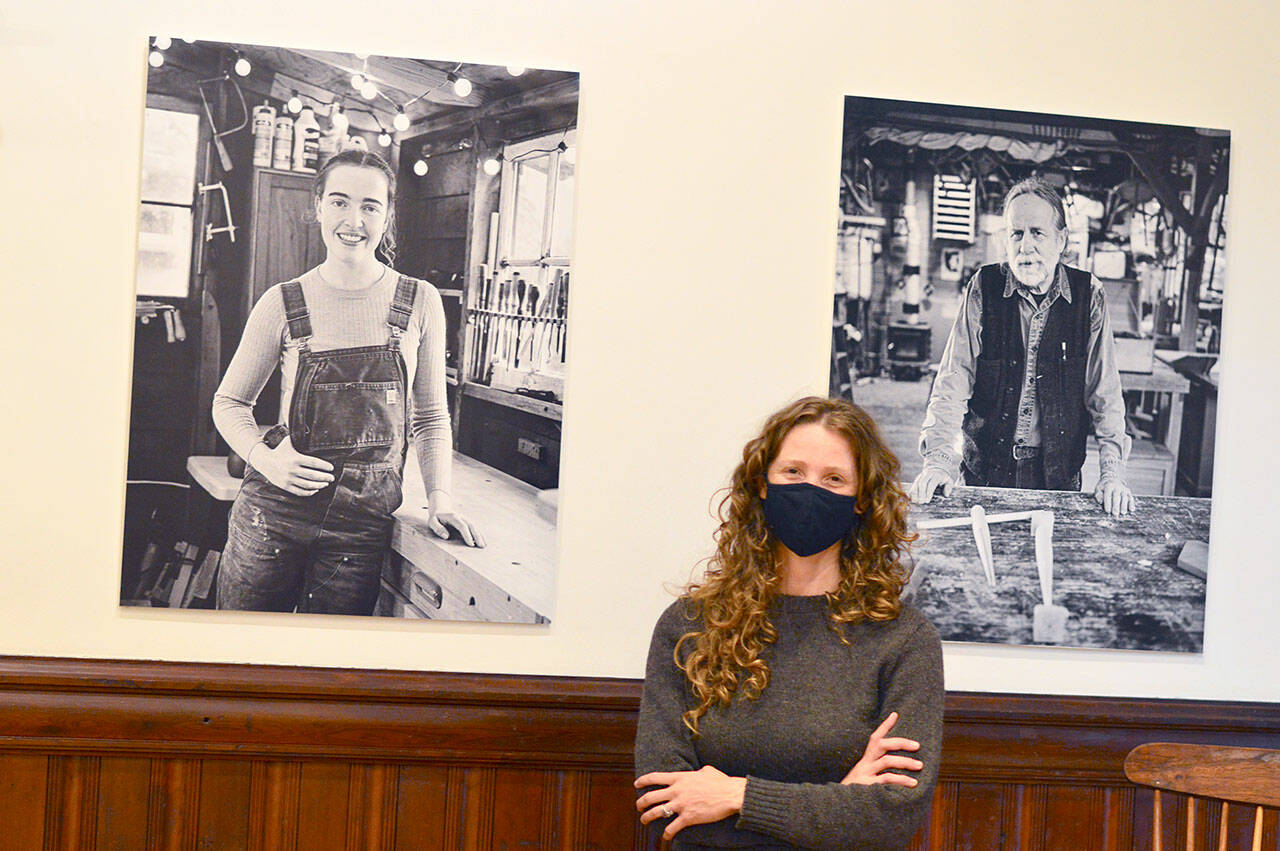 Inside the Jefferson Museum of Art & History’s “Wood” exhibition, executive director Shelly Leavens stands between portraits of woodworkers Annalise Rubida and Steve Habersetzer. (Diane Urbani de la Paz/Peninsula Daily News)