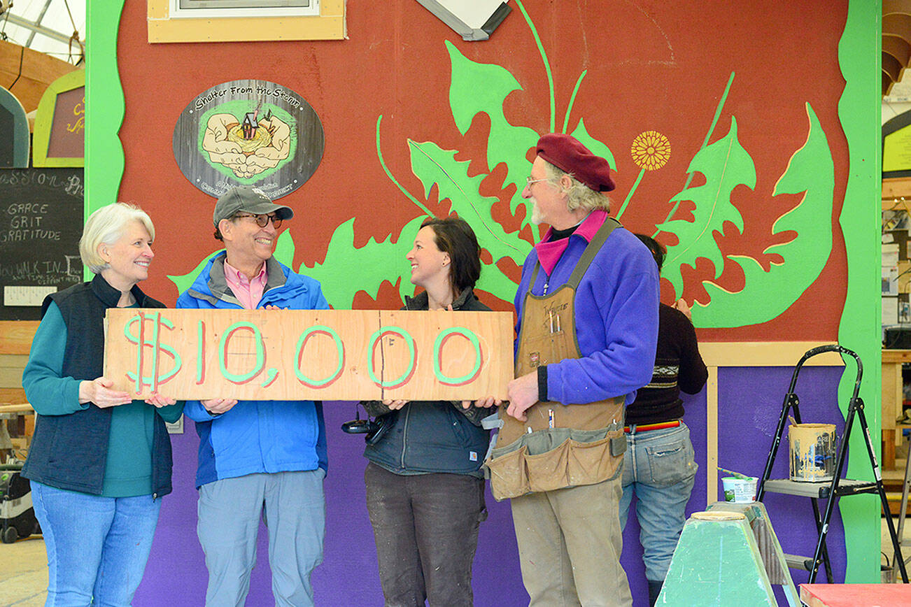 To mark the Rotary Club of Port Townsend's $10,000 gift to the Community Boat Project -- which is constructing tiny homes for local farmworkers -- boat project director Wayne Chimenti, far right, and shop organizer Gillian Kenagy, second from right, quickly painted a "check" on a piece of wood. Rotarian Carla Caldwell, far left, and club president Jim Cunnington were among the volunteers who joined a work party toward finishing the project's latest wooden tiny house last week.  Diane Urbani de la Paz/Peninsula Daily News