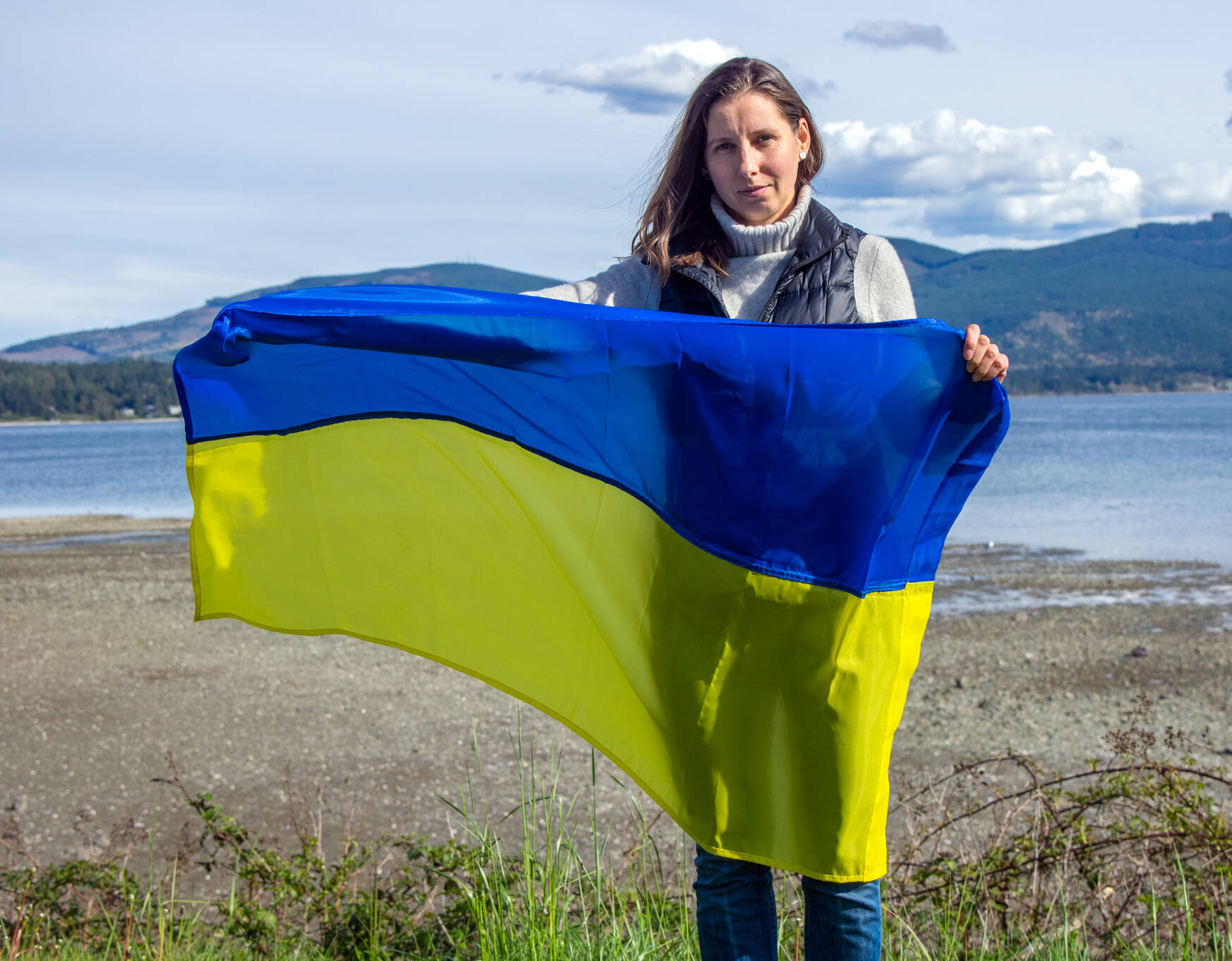 Ukrainian-American Mariia Bush holds the Ukranian flag up at the John Wayne Marina in Sequim as she discusses the upcoming “Ukraine at the Table” benefit to be held at Bella Italia on Tuesday. (Emily Matthiessen/Olympic Peninsula News Group)