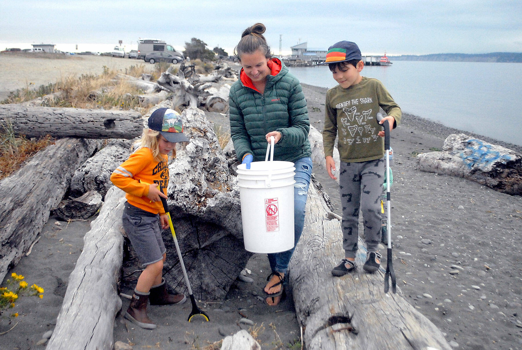 Tegan Glaude of Port Angeles, center, along with 5-year-old Wolf Schultz-Wade, left, and Odin Glaude, 6, pick up trash in the driftwood along Ediz Hook in Port Angeles as part a beach cleanup effort in 2021. The event was hosted by CoastSavers and the Olympic Peninsula Chapter of the Surfrider Foundation. (Keith Thorpe/Peninsula Daily News)