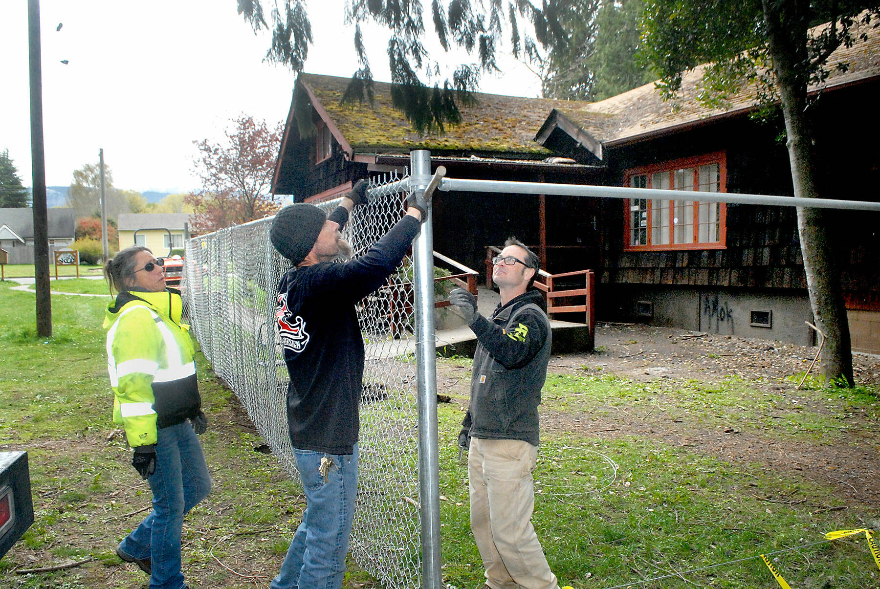 Port Angeles Parks and Recreation Department workers, from left, Brooke Keohokalole, Darryl Anderson and Eli Hammel install a chain link fence around a portion of the Campfire Clubhouse at Jessie Webster Park on Wednesday. (Keith Thorpe/Peninsula Daily News)