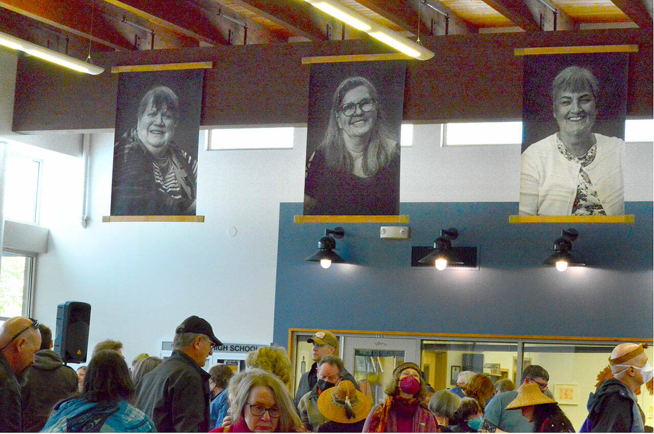 Veillant sur la foule à l'ouverture de l'exposition « Still Here » au Chimacum School Commons, les portraits de Brian Goodman de, de gauche à droite, Carol Plaster, Renita Meyer Gromley et Mary Anne Gentry.  (Diane Urbani de la Paz/Peninsula Daily News)