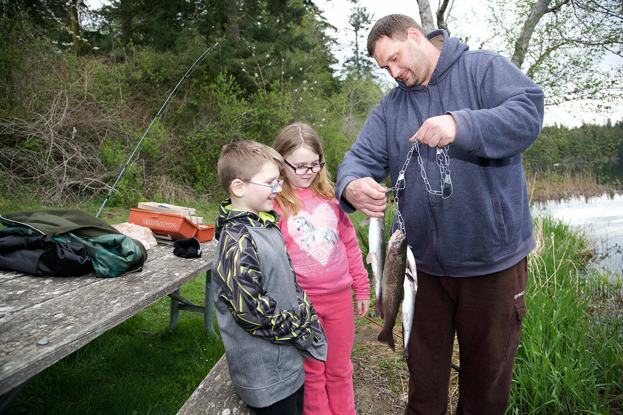 Jim Dunn, from Port Orchard, show off his trout catch to son, Joshua, 8, and daughter Alia, 10, while fishing on the opening day of trout fishing at Anderson Lake. (Steve Mullensky/for Peninsula Daily News)