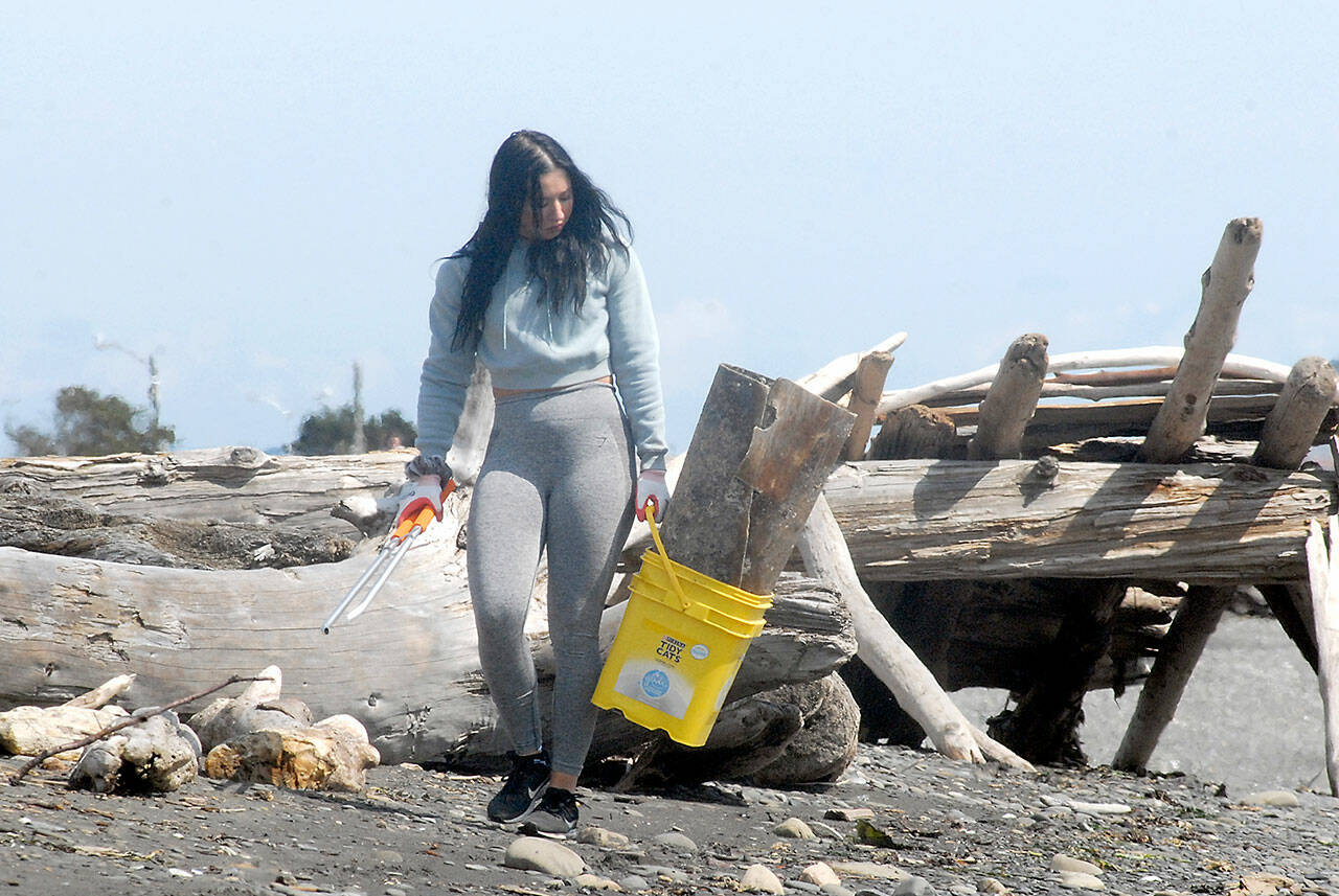 Chynna Penird of Port Angeles collects trash and debris from the driftwood along Ediz Hook in Port Angeles on Saturday as part of a beach cleanup effort in honor of Earth Day. The event, hosted by Washington CoastSavers with assistance from other groups and supporters, drew more than two dozen participants. (Keith Thorpe/Peninsula Daily News)