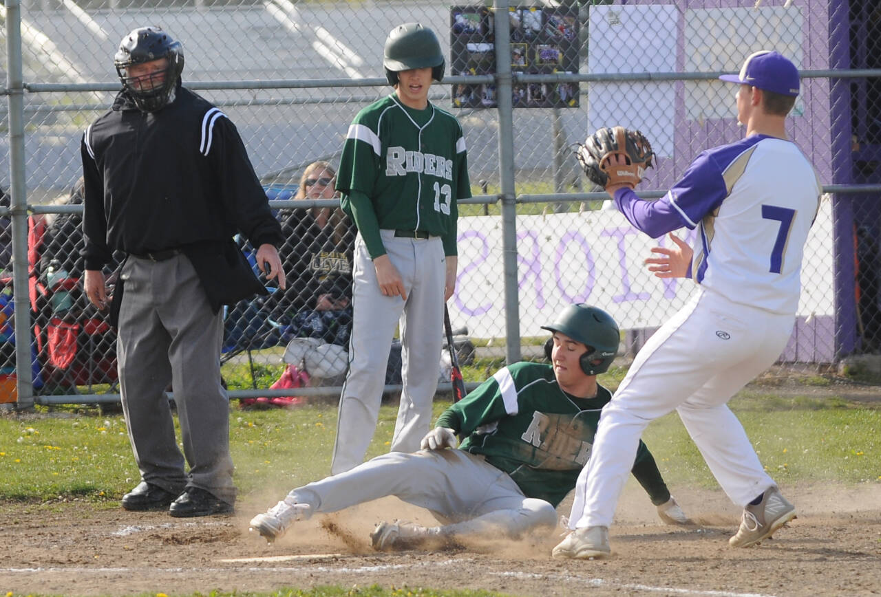 With teammate Hunter Robinson (13) looking on, Port Angeles' Colton Romero slides safely into home ahead of the tag of Sequim pitcher Connor Bear in Sequim on Monday. (Michael Dashiell/Olympic Peninsula News Group)