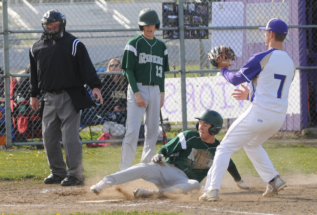 With teammate Hunter Robinson (13) looking on, Port Angeles Colton Romero slides safely into home ahead of the tag of Sequim pitcher Connor Bear in Sequim on Monday. (Michael Dashiell/Olympic Peninsula News Group)