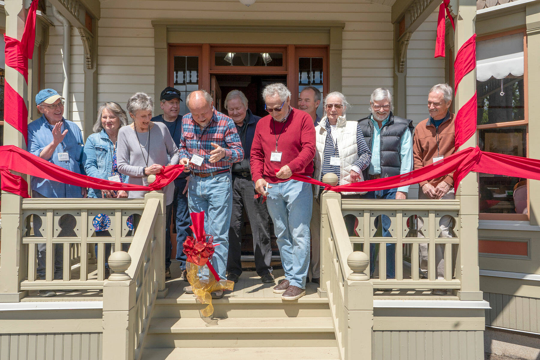 <address>Chair of the Board Christine Satterlee, left, holds the ribbon as Project managers David Satterlee, left, and Chuck Thrasher wield scissors to cut the ribbon to signal the restoration of the 130 year old Worthington House is complete and open to the public. The cutting took place in Quilcene on Friday. (Steve Mullensky/for Peninsula Daily News)</address>