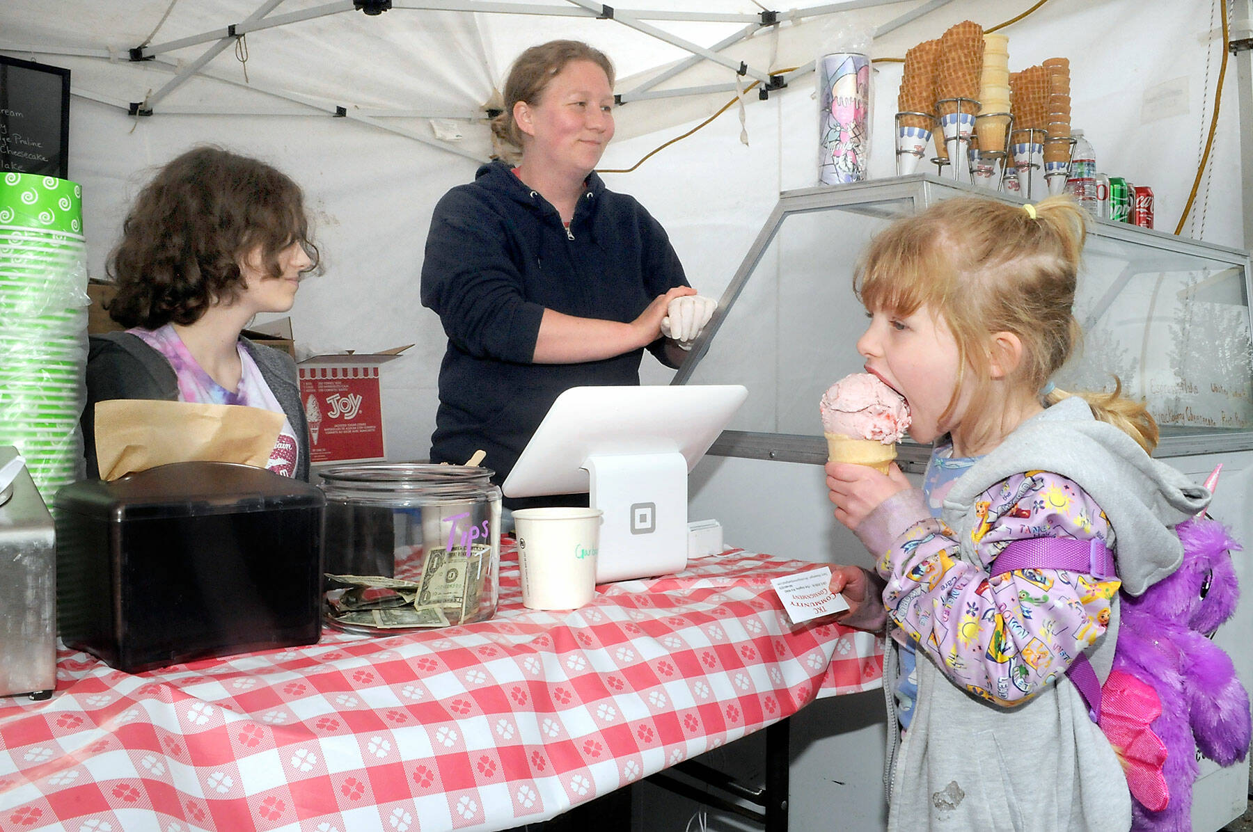 Alana Black, center, and her daughter, Sophia Strickland, 14, left, operate their Skokomish Valley-based Olympic Mountain Ice Cream tent while 5-year-old Evelyn Bonebreak of Port Angeles enjoys a cone on Friday at the Juan de Fuca Festival of the Arts in Port Angeles. (Keith Thorpe/Peninsula Daily News)